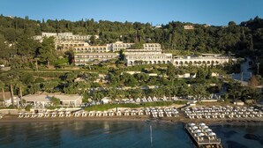 Un complejo turístico frente al mar con varias edificaciones, un puerto deportivo y una zona de playa con sombrillas.