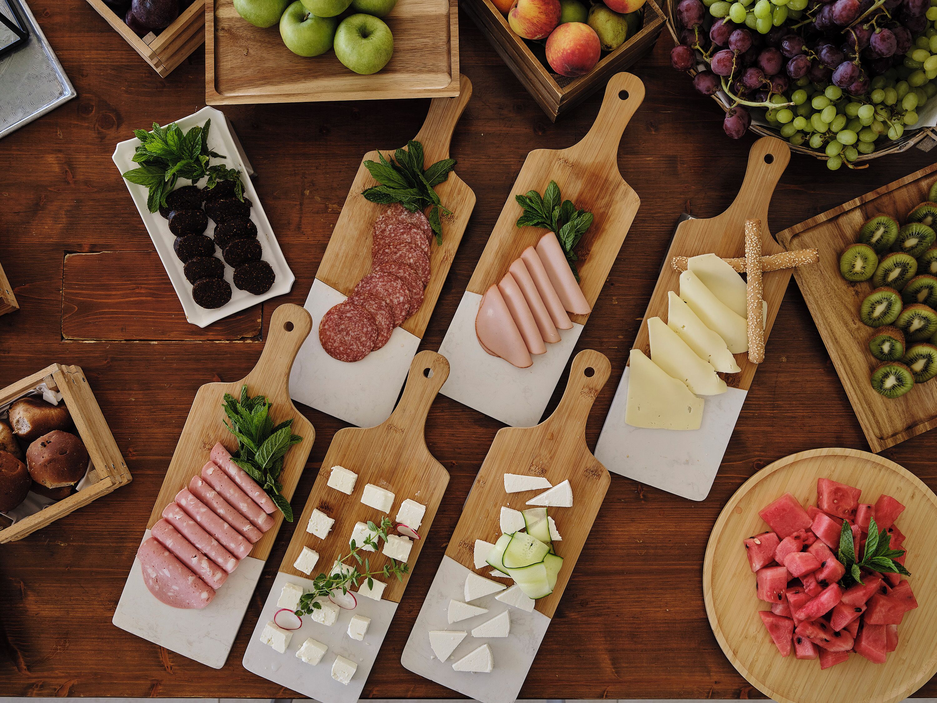 A wooden table with various food items like sliced meats, cheeses, fruits, and vegetables.
