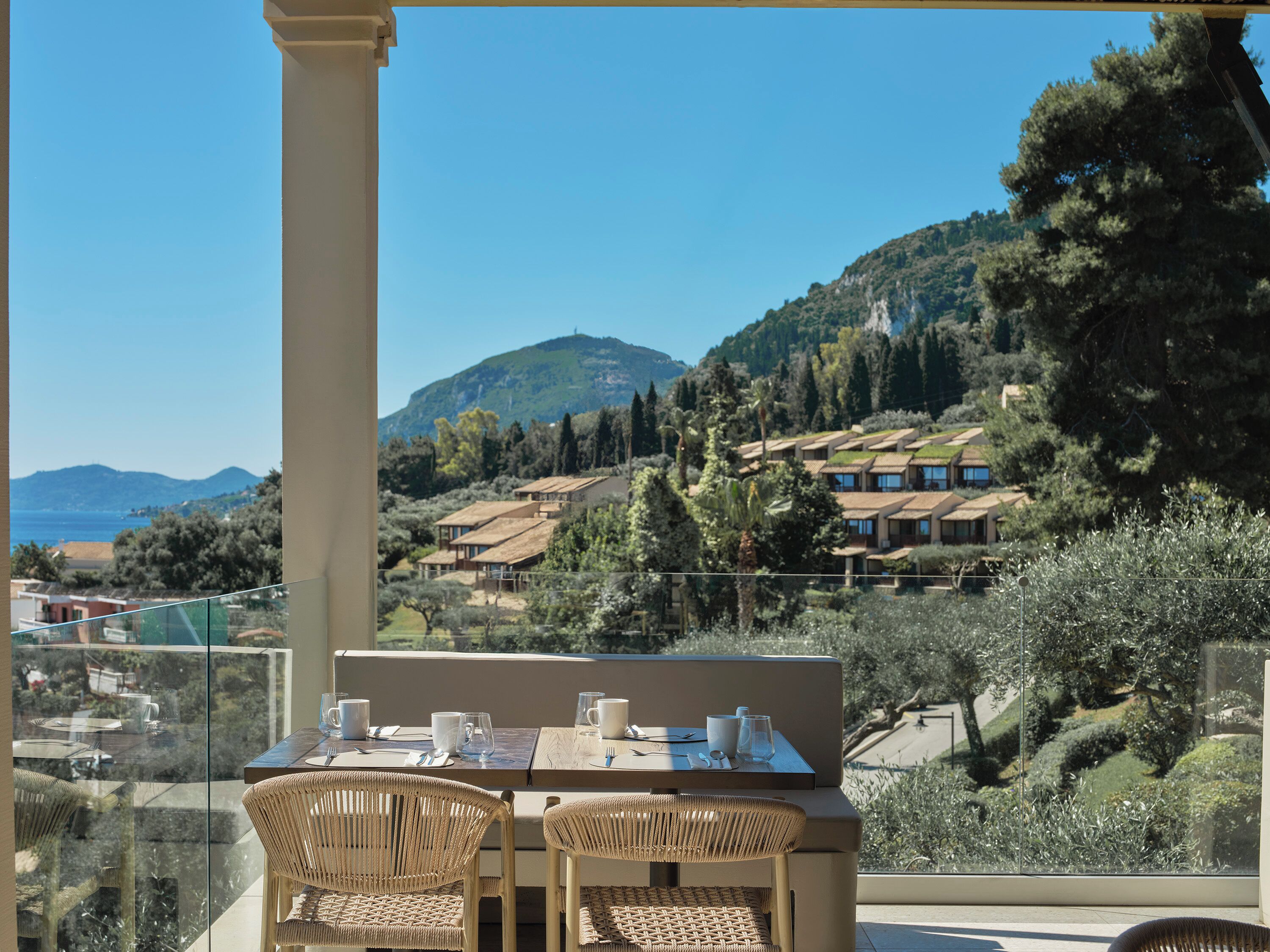 A terrace with a table set for two, overlooking a scenic hillside with houses and trees.