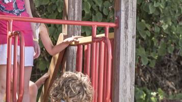 A child on a wooden slide with metal railings, surrounded by greenery.