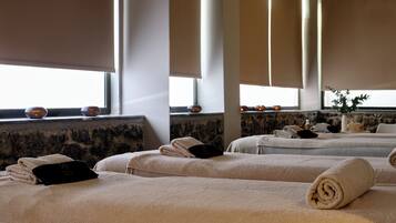 A spa room with multiple massage tables, each with a rolled towel and a black card.