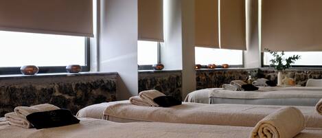 A spa room with multiple massage tables, each with a rolled towel and a black card.