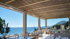 Un espacio de estar al aire libre techado, con mesas y sillas, con vistas panorámicas al mar y las colinas.