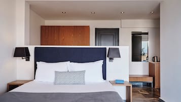 A modern hotel room with a large bed, two bedside lamps, a wooden headboard, a small wooden nightstand, and a view of the outside through a door.