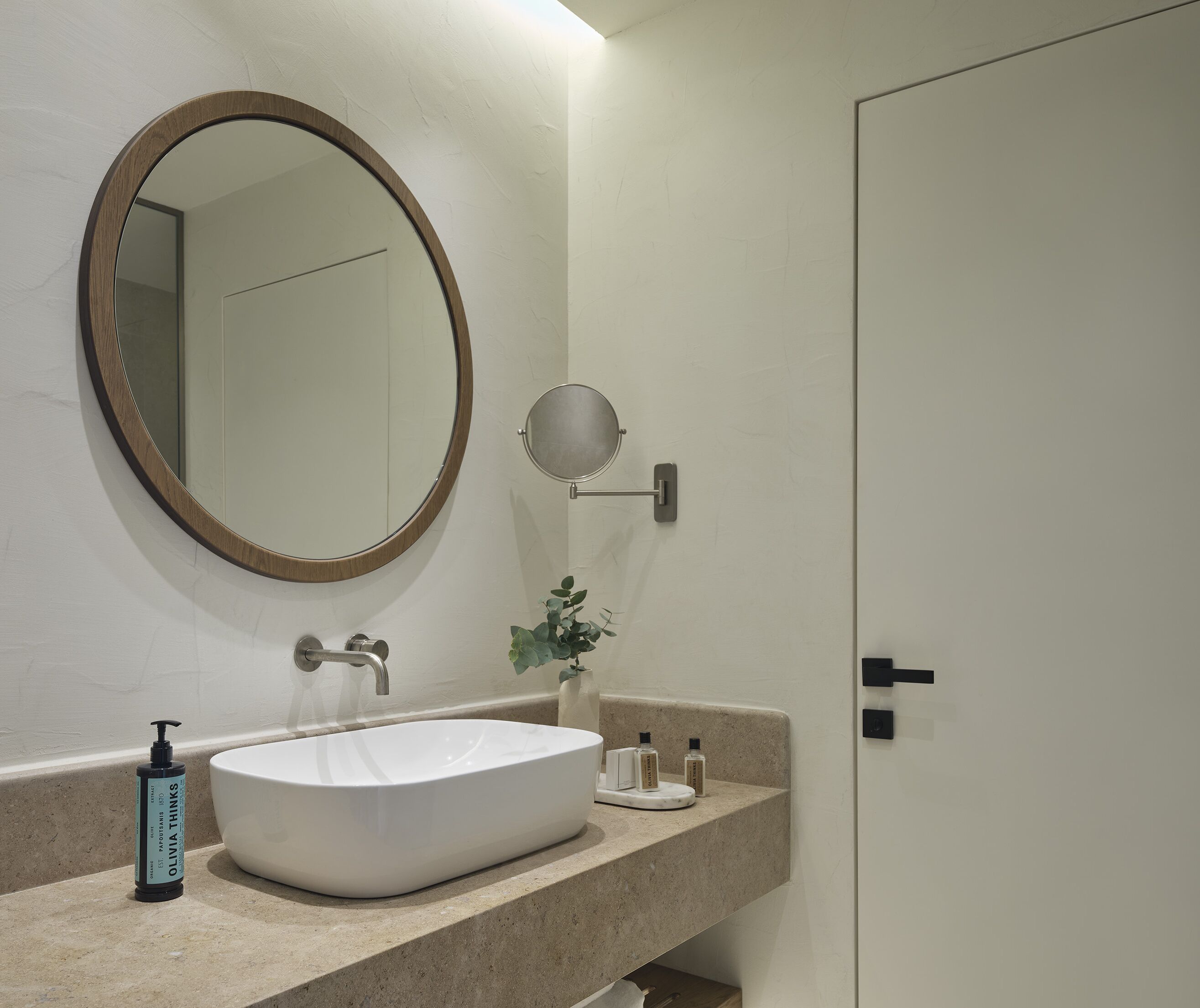 A bathroom with a white sink, a round mirror, a small round mirror, a bottle of soap, and a door.