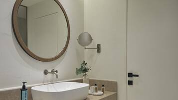 A bathroom with a white sink, a round mirror, a small round mirror, a bottle of soap, and a door.