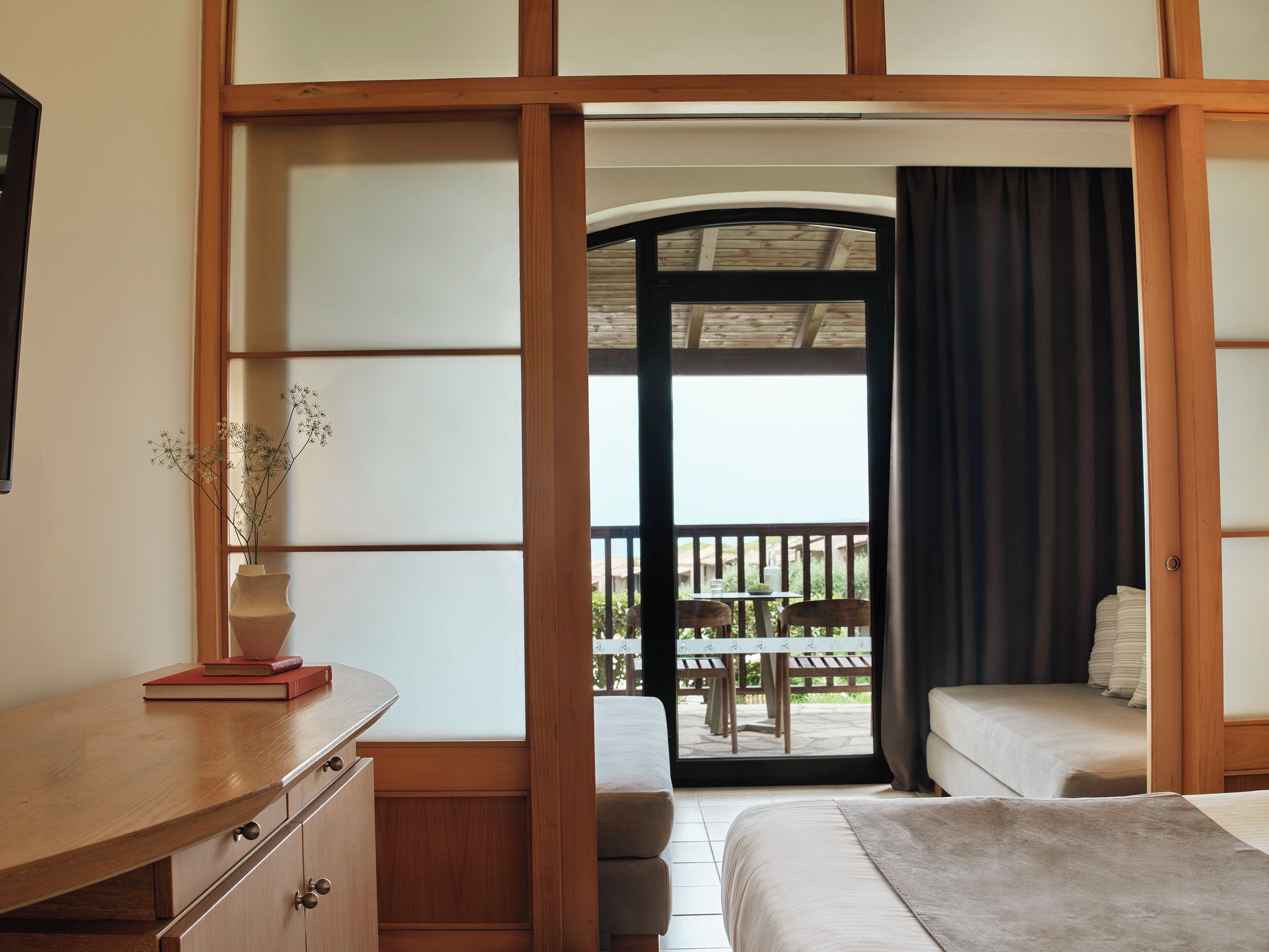A bedroom with a wooden desk, a bed, and a view of an outdoor balcony.