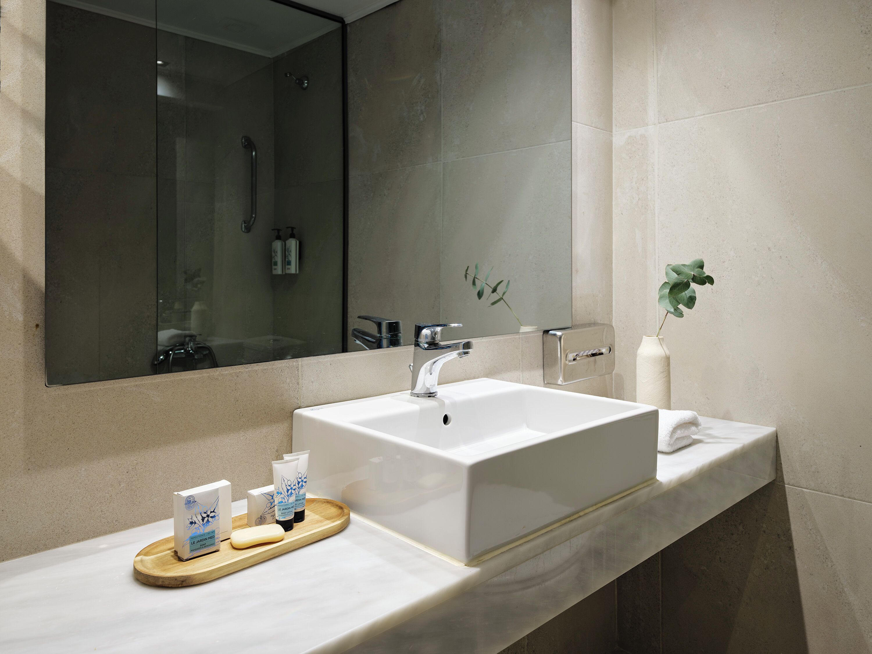 Un bagno moderno con uno specchio grande, un lavandino bianco e un vassoio di legno con articoli da toilette.