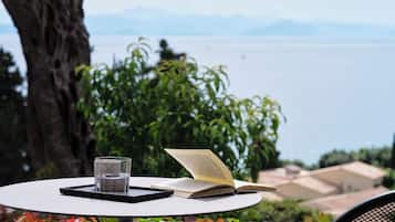 A table with a book and a glass of water, set against a backdrop of greenery and a view of the sea.