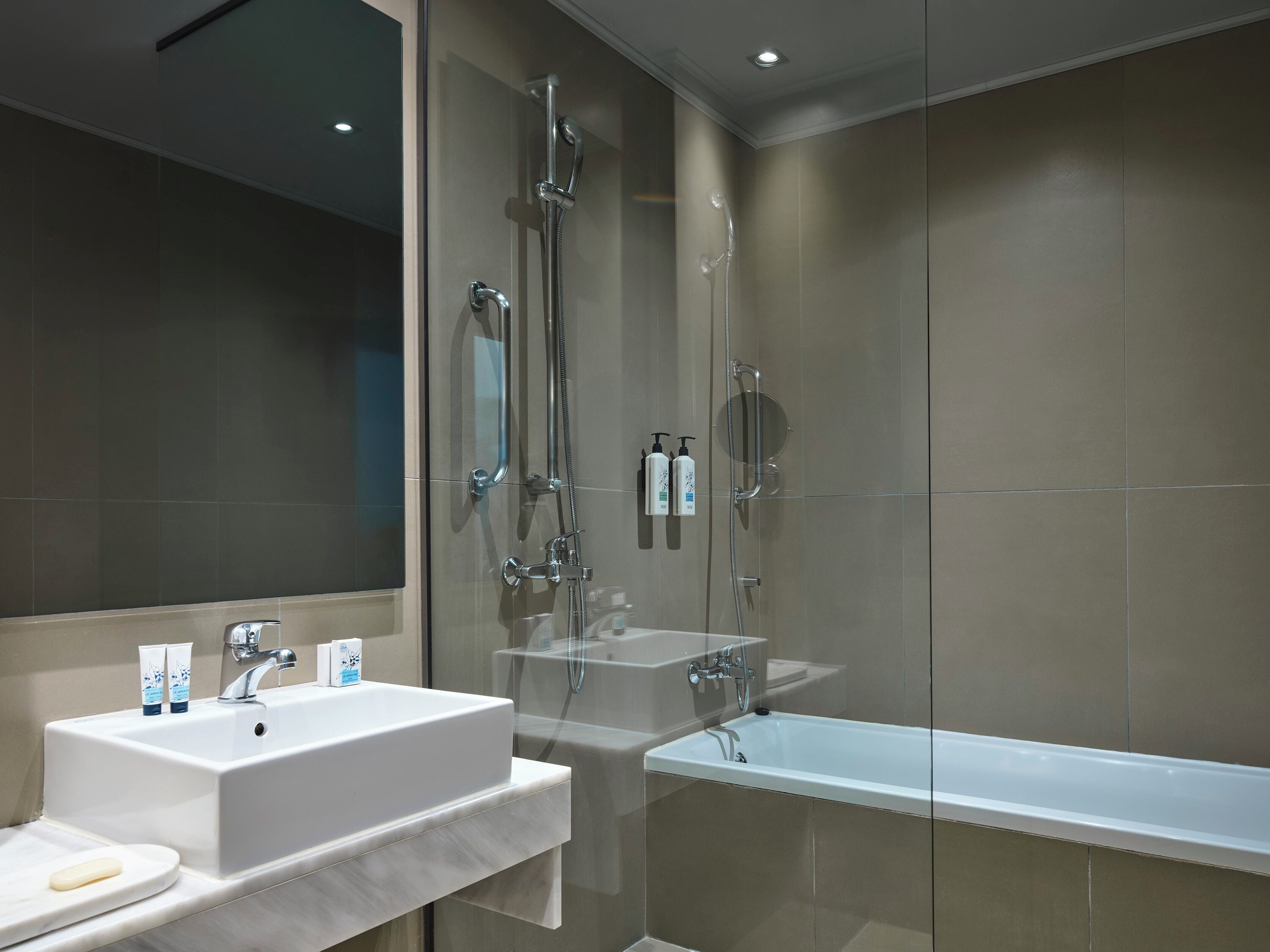 A modern bathroom with a glass-enclosed shower, a white sink with a mirror, and a white bathtub.