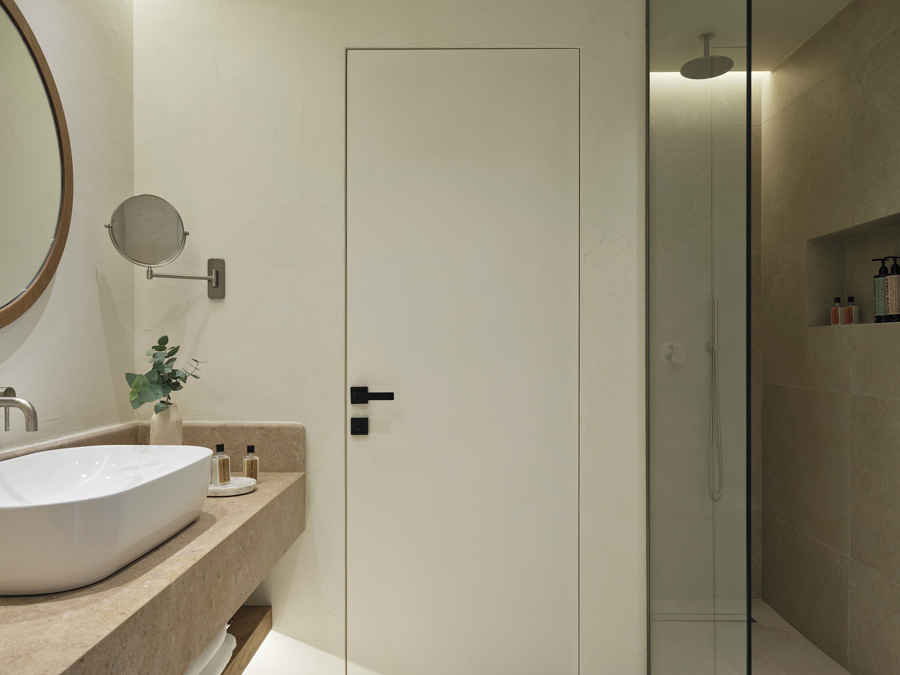 A modern bathroom with a large white sink, a round mirror, and a glass-enclosed shower.