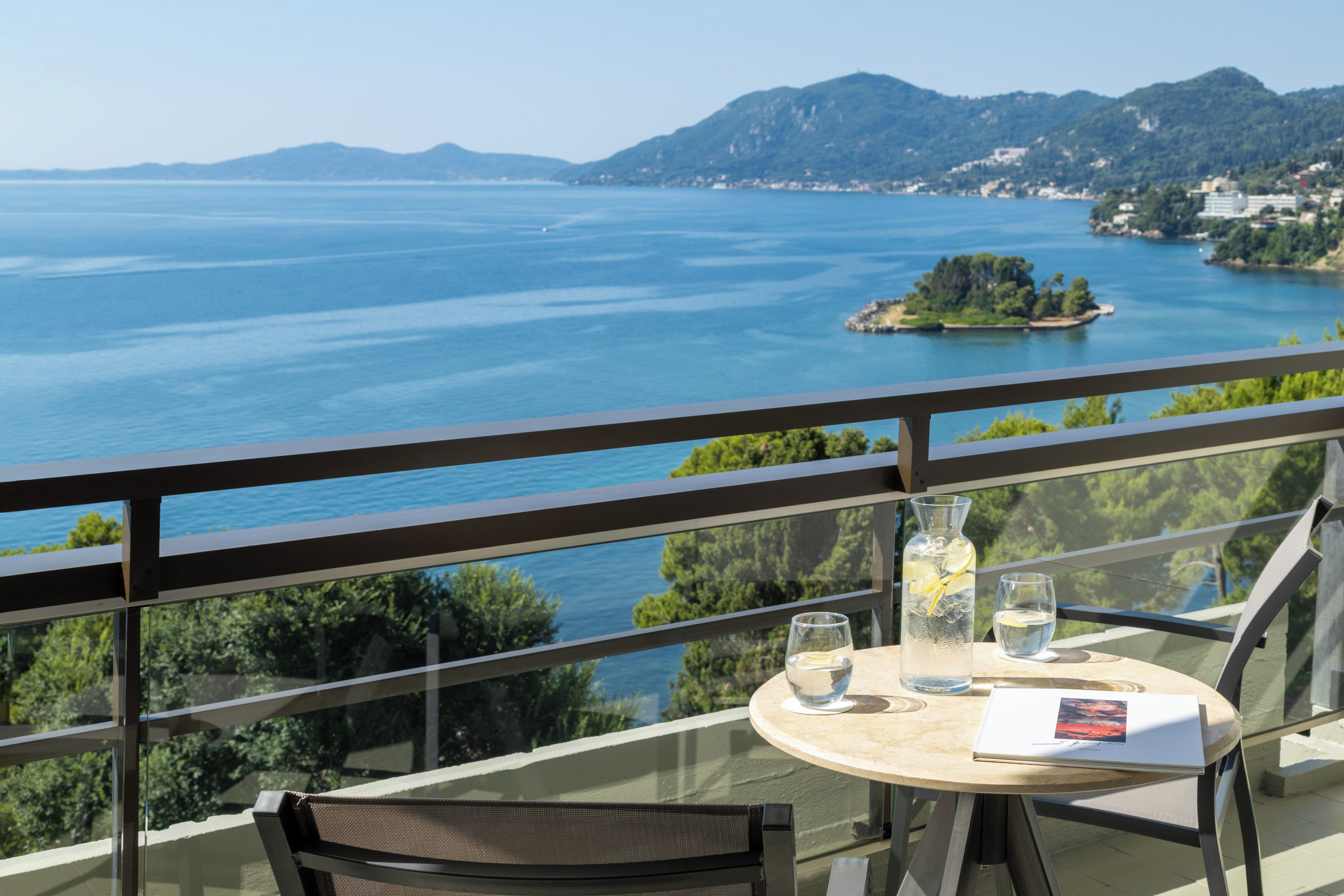 A balcony with a table, a chair, a glass of water, a bottle with a lemon slice, and a book.