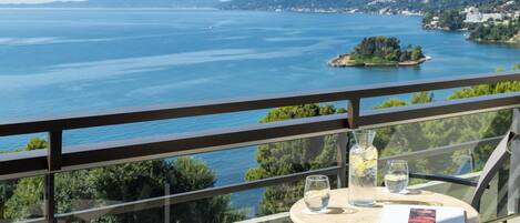 A balcony with a table, a chair, a glass of water, a bottle with a lemon slice, and a book.