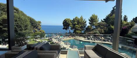 A covered outdoor seating area with wicker furniture, a pool, and a view of the sea.