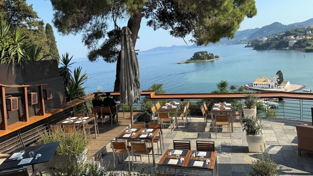 Un área de comedor al aire libre con mesas y sillas, con vista a un cuerpo de agua y una pequeña isla.