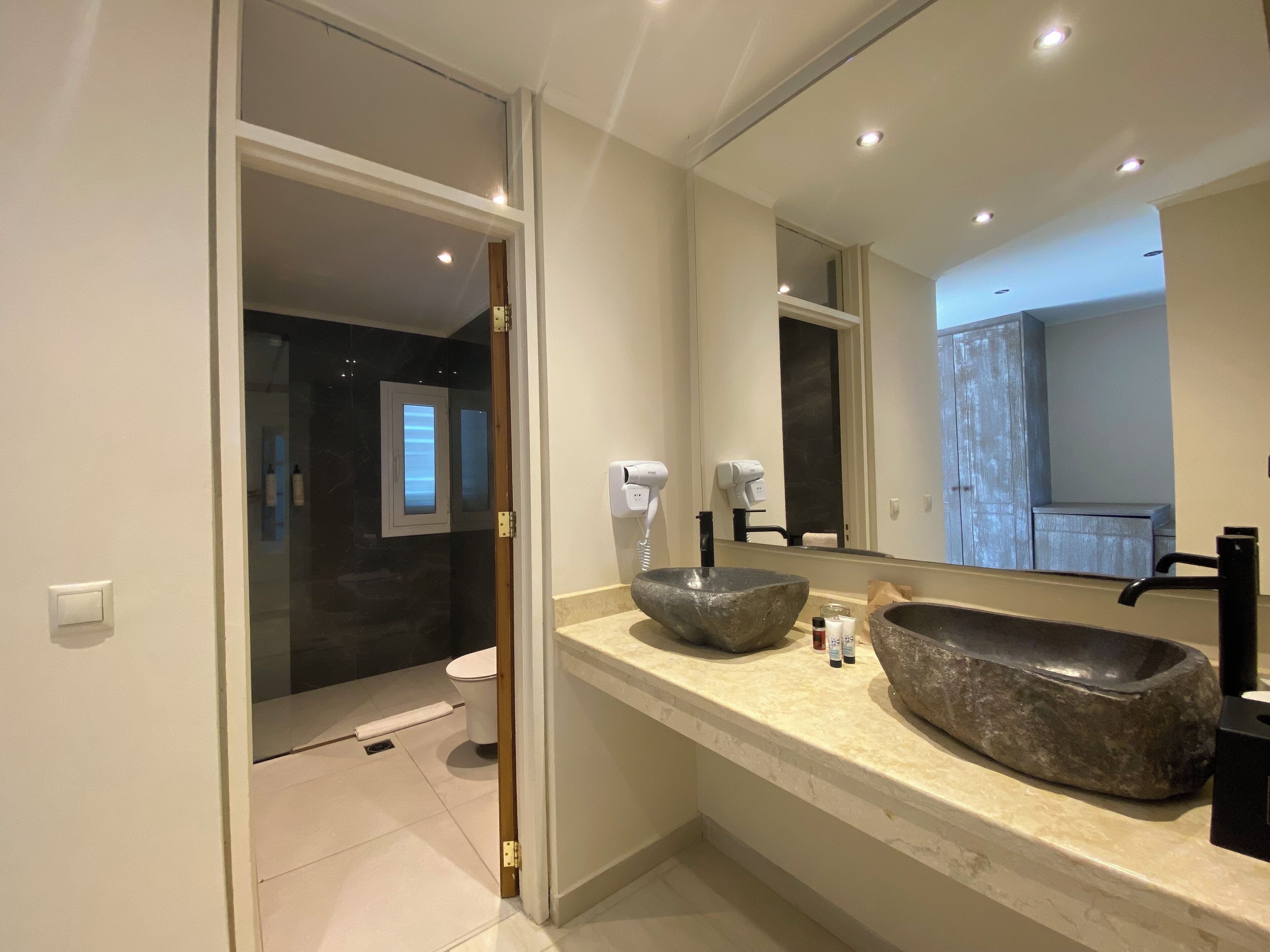 A modern bathroom with a large mirror, a stone sink, and a toilet visible through a glass door.