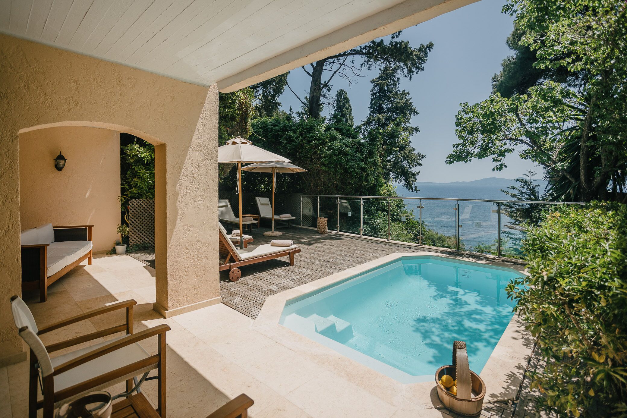 A pool area with lounge chairs, a table, and a view of the sea.