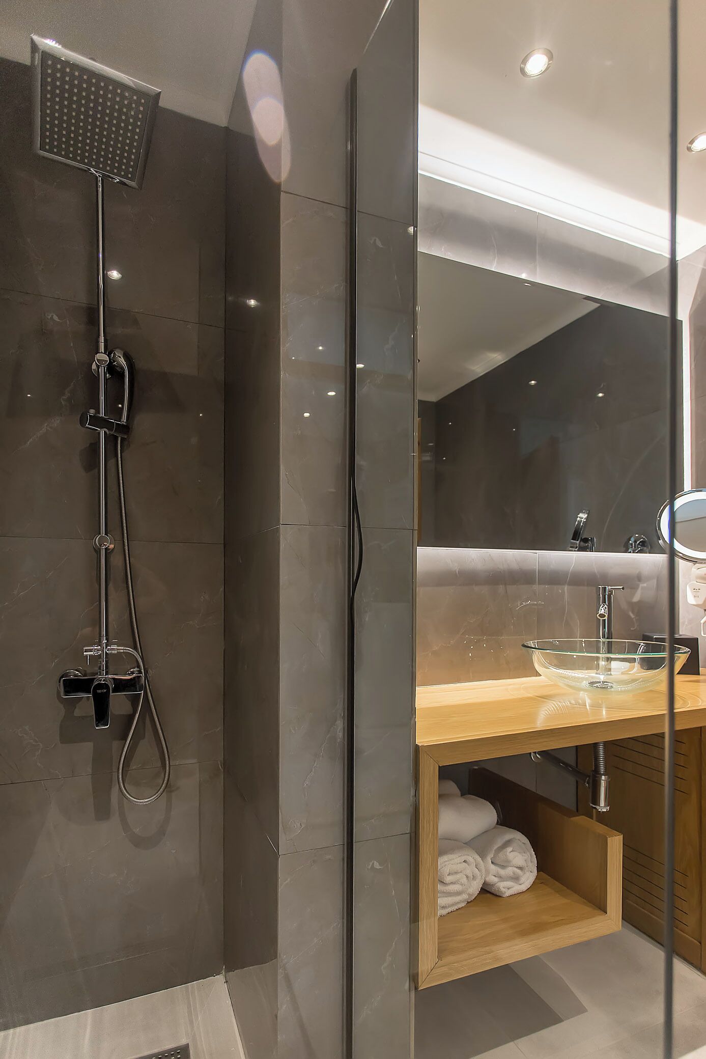 A modern bathroom with a glass-enclosed shower, a wooden vanity with a glass bowl sink, and a mirror above the sink.