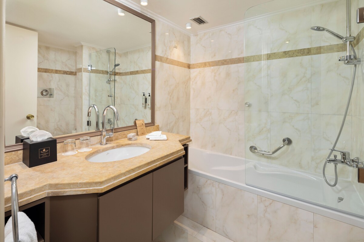 A modern bathroom with a marble sink, a large mirror, a glass-enclosed shower, and a bathtub.