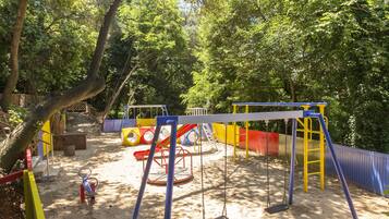 Un’area giochi con altalene, scivoli e strutture per arrampicarsi, circondata da alberi.