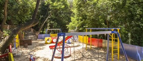 A playground with swings, slides, and climbing structures surrounded by trees.