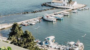 Un puerto costero con barcos amarrados, una pequeña isla y un edificio blanco con techo rojo.