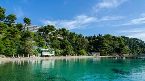 Una zona costera con agua turquesa cristalina, una playa con sombrillas y un edificio con una escalera que lleva a él.