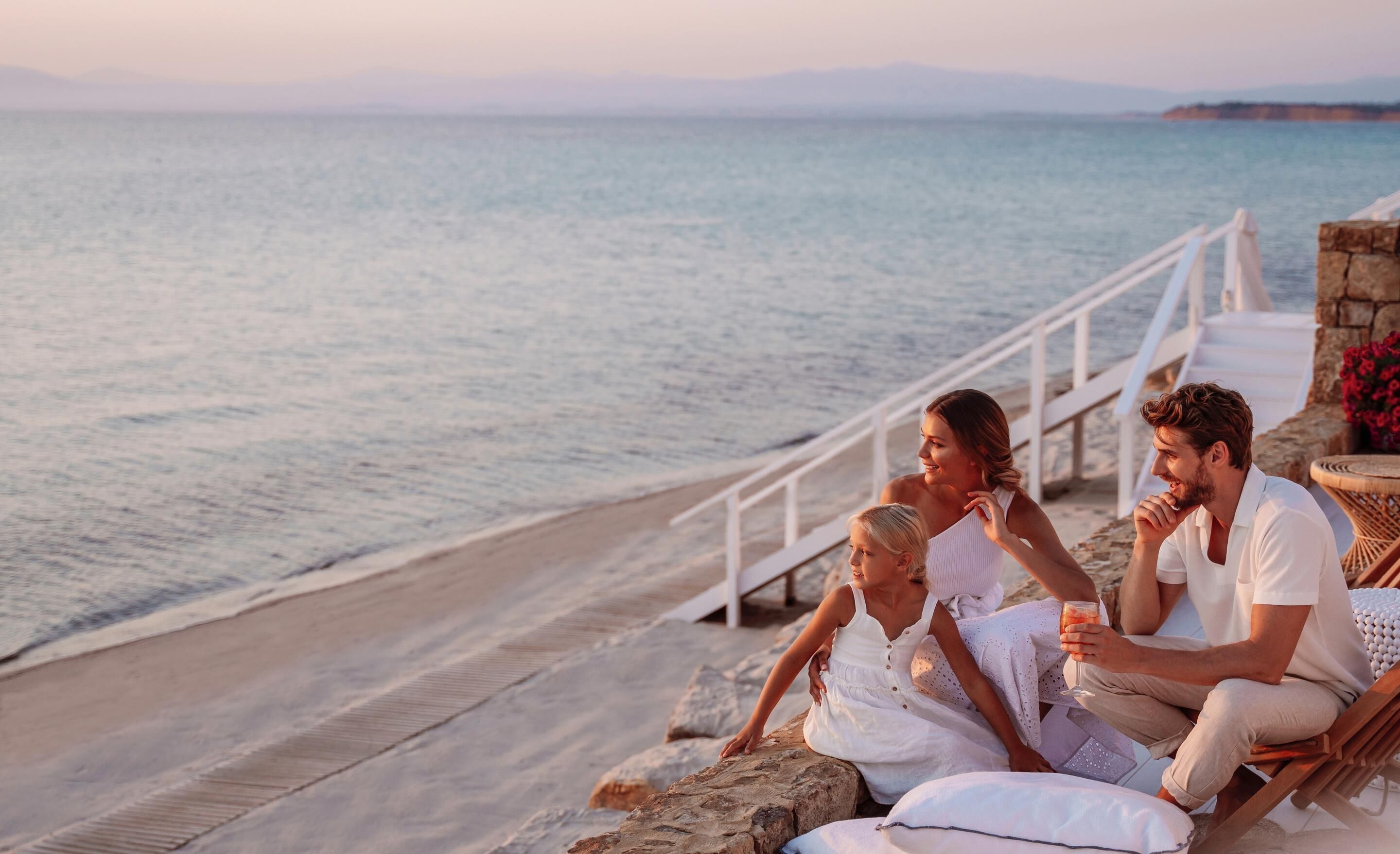 A family of four on a wooden deck overlooking a beach with a railing and a stone wall.