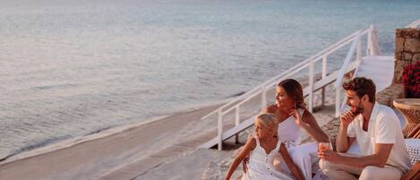 A family of four on a wooden deck overlooking a beach with a railing and a stone wall.
