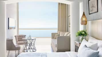 A modern hotel room with a balcony, a bed, a seating area, and a view of the sea.