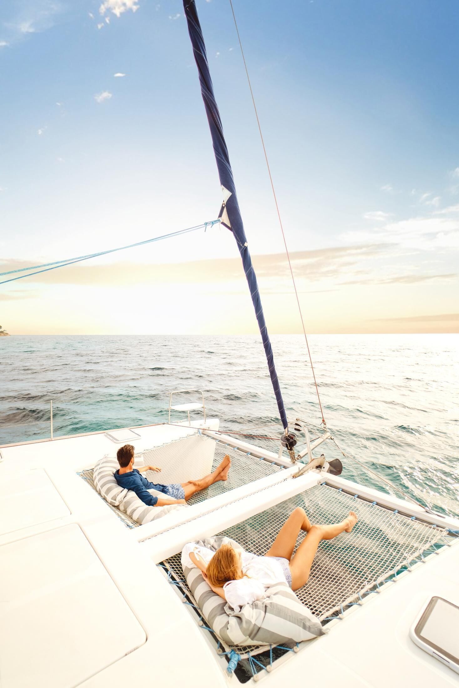 A sailboat with two people lying on deck chairs, facing the sea.