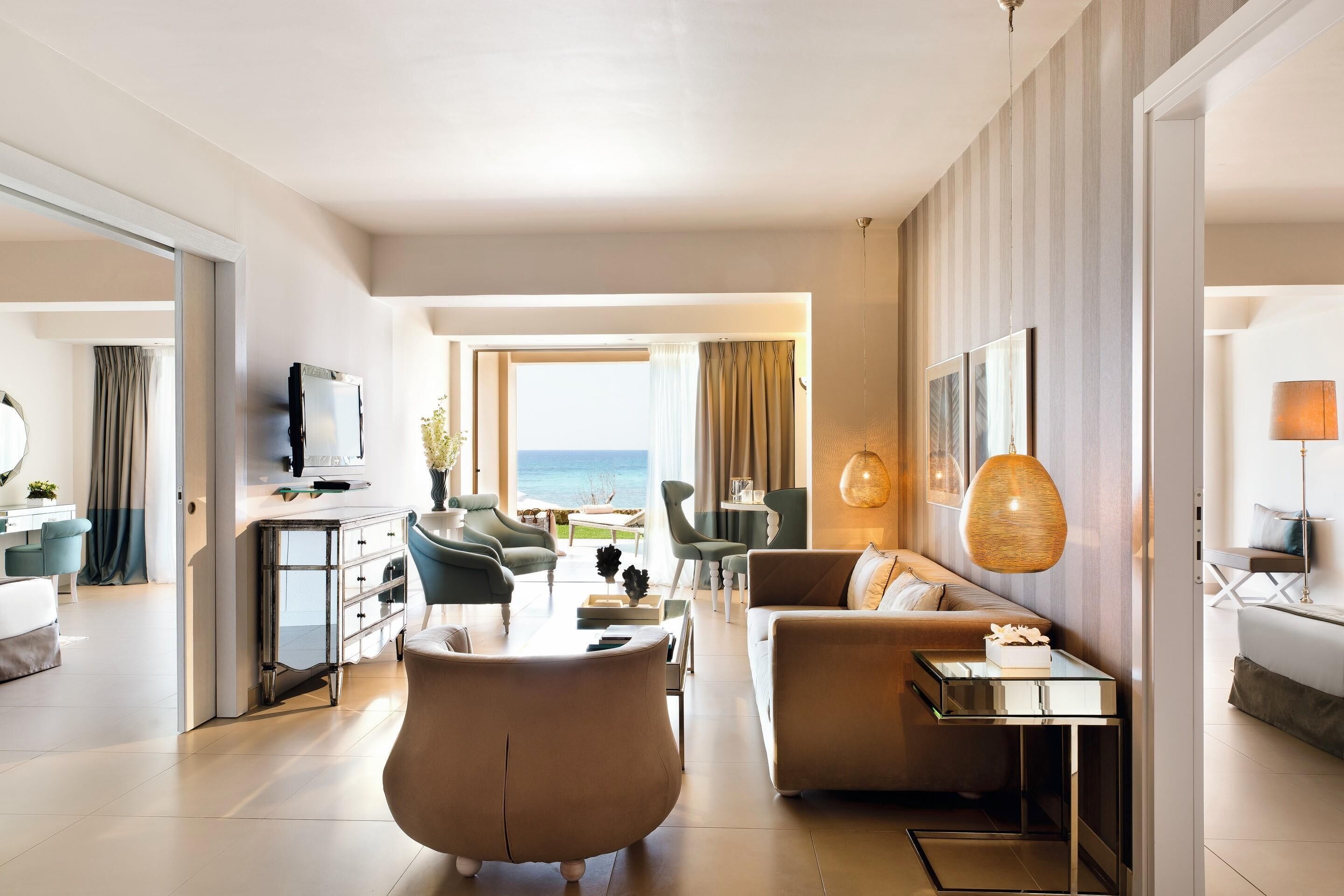 A modern hotel room with a living area, a sofa, a coffee table, and a TV.
