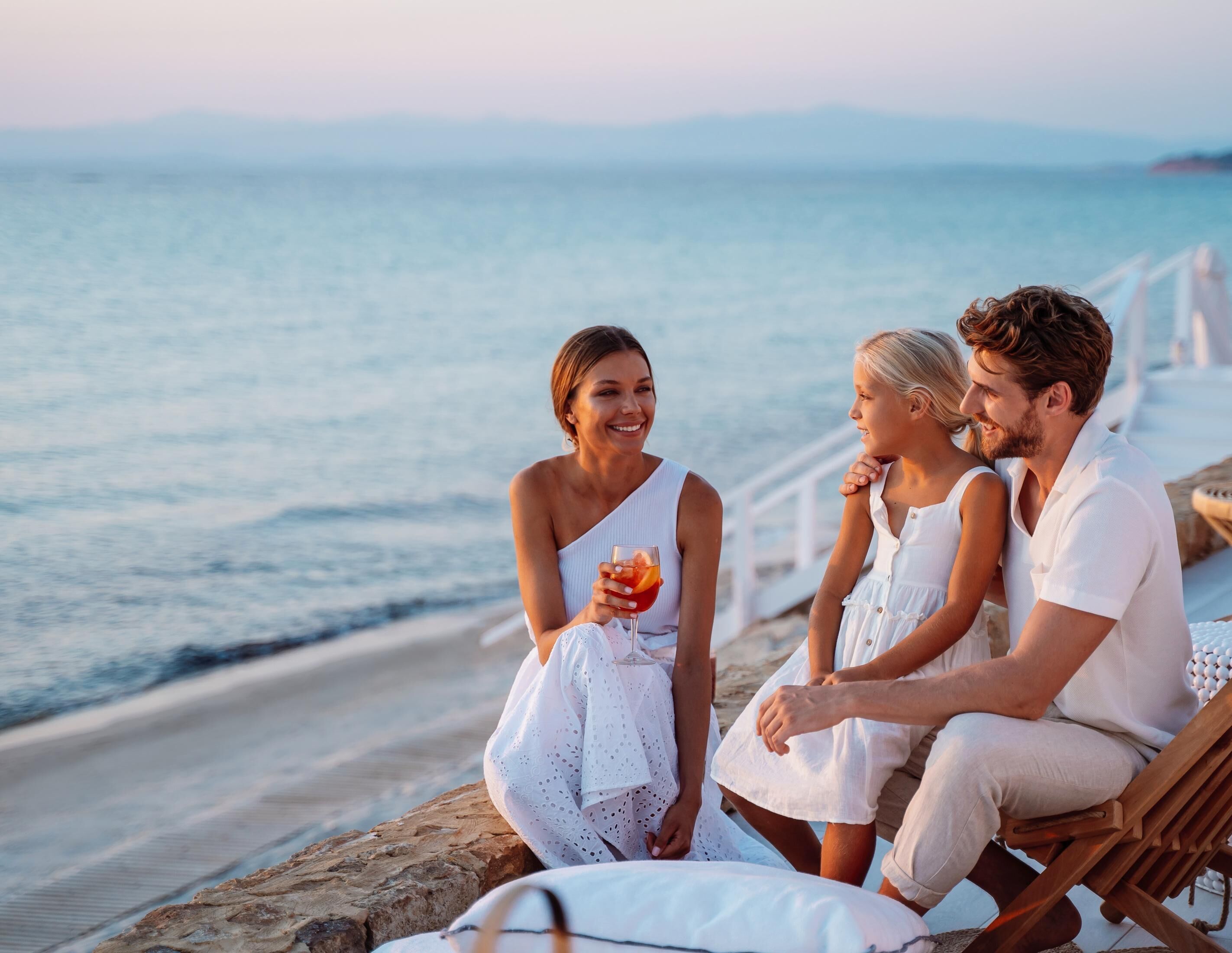 A couple and two children sitting on a wooden bench by the seaside, overlooking the ocean.