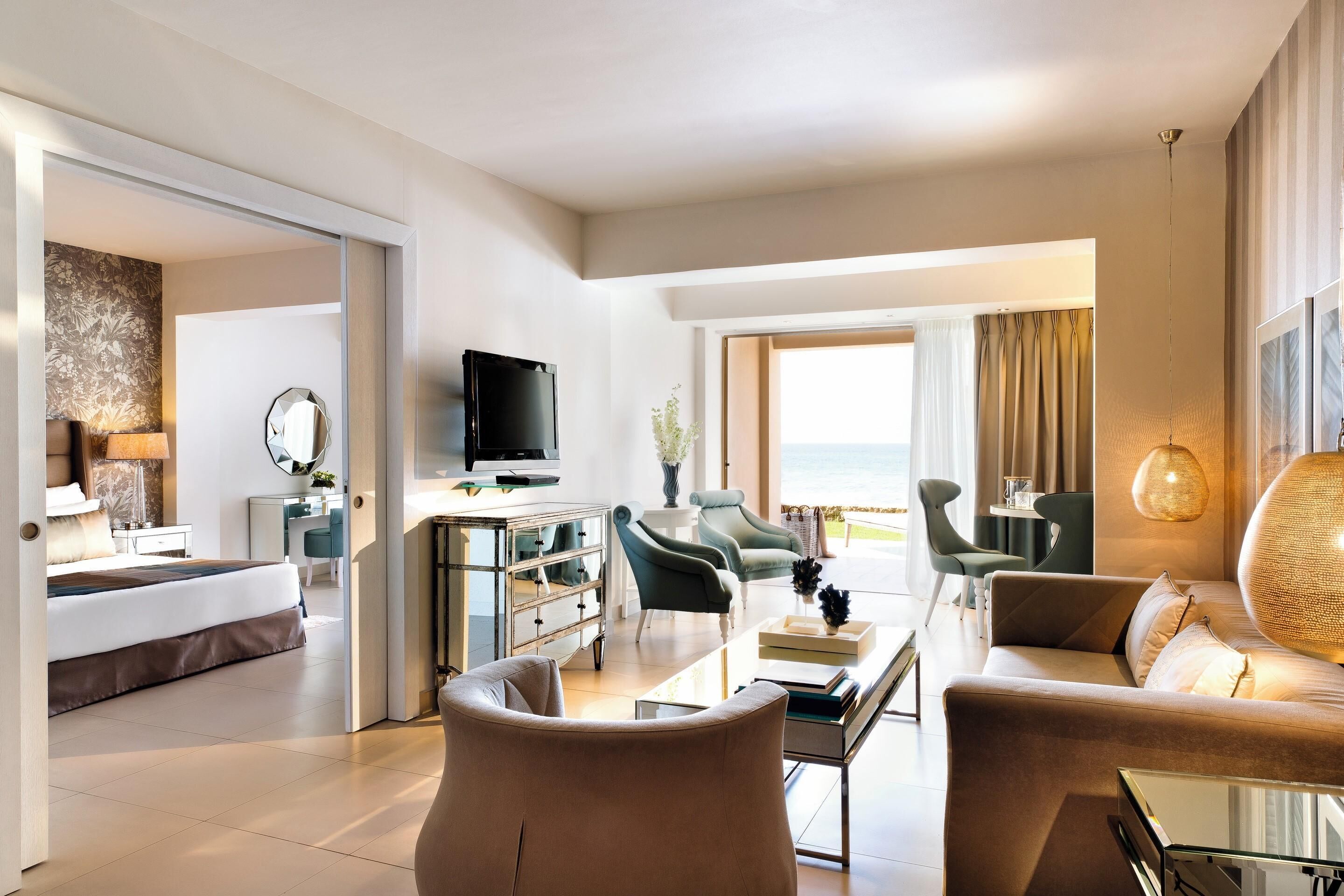 Ein modernes Hotelzimmer mit Bett, Sitzecke, Fernseher und Blick ins Freie.
