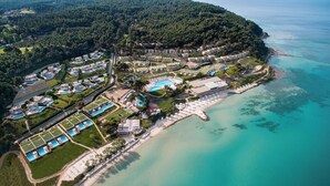 An aerial view of a coastal resort with multiple swimming pools, a beach, and a forested peninsula.