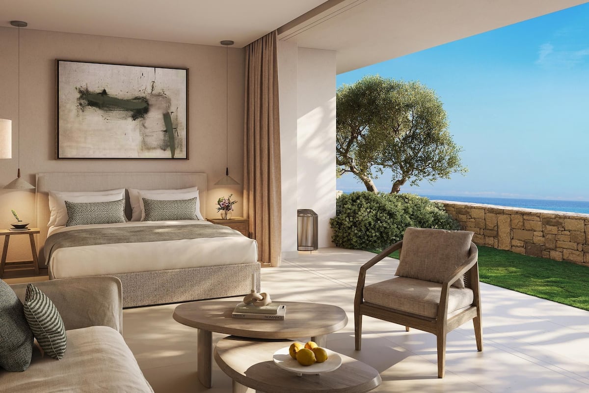 Quarto moderno com uma cama grande, um sofá, uma mesa de centro e vista para o mar.