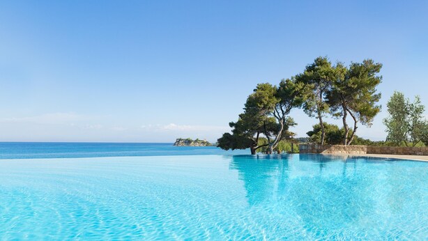 A clear blue infinity pool with a view of the sea and trees.