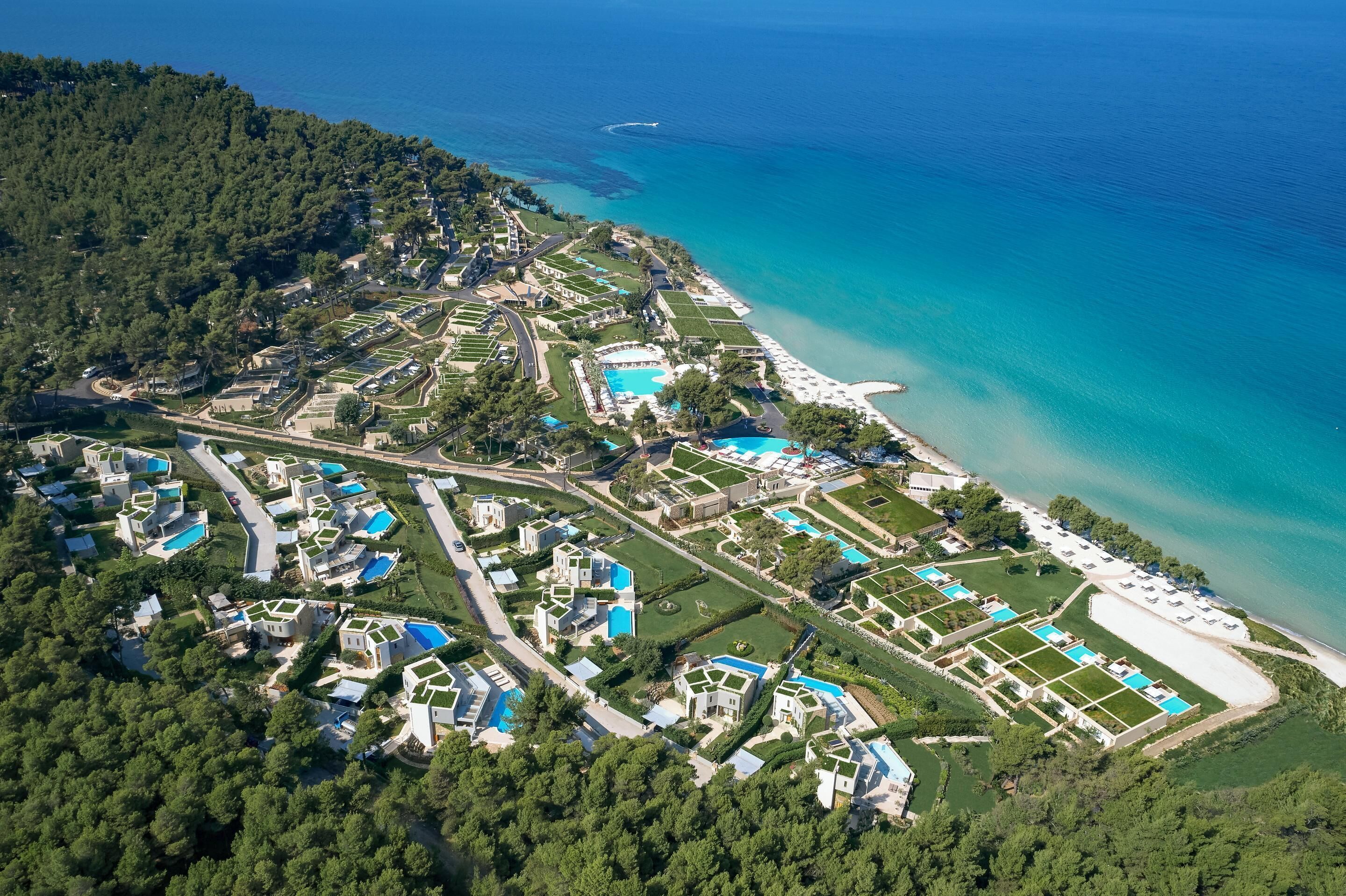 An aerial view of a coastal resort with multiple swimming pools, a beach, and lush greenery.