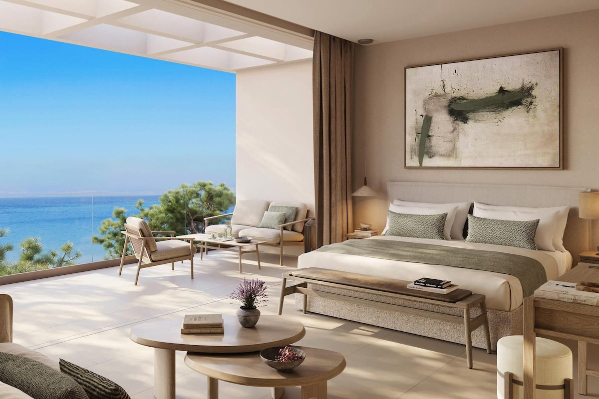 Quarto espaçoso com uma cama grande, área de estar com mesa de centro e vista para o mar.