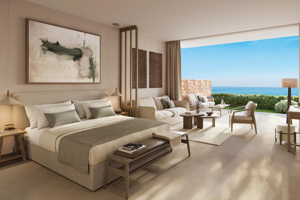 Quarto moderno com uma cama grande, um sofá, uma mesa de centro e vista para o oceano.