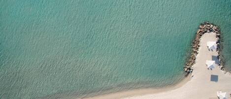 An aerial view of a beach with a row of white umbrellas and a rocky breakwater.