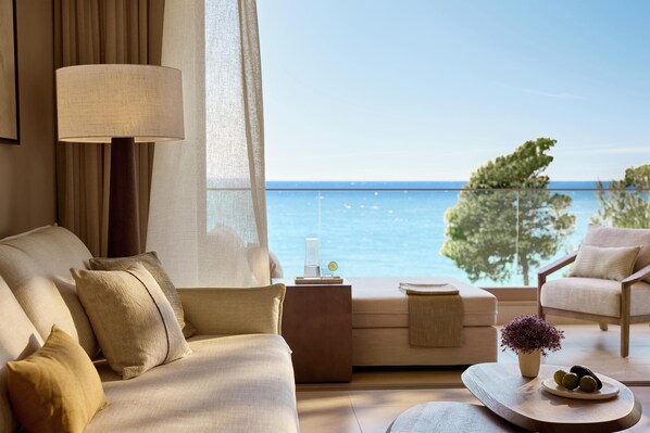 A room with a sofa, a chair, a lamp, a small table with a plant, and a view of the sea. - Sani Club (Kassandra)