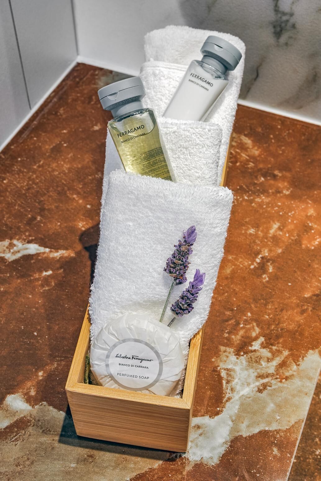 A wooden box containing a white towel, a bottle of Ferragamo perfume, and a lavender sprig.