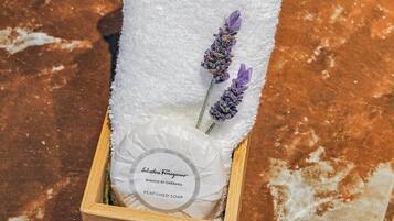 A wooden box containing a white towel, a bottle of Ferragamo perfume, and a lavender sprig.