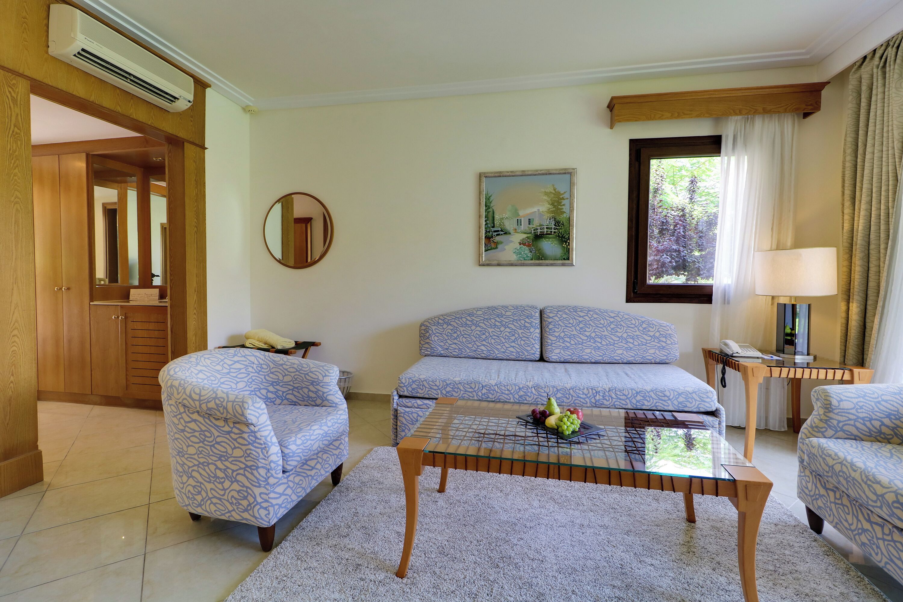 A living room with patterned sofas, a glass coffee table with fruit, a painting, and a wooden door.