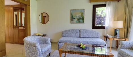 A living room with patterned sofas, a glass coffee table with fruit, a painting, and a wooden door.
