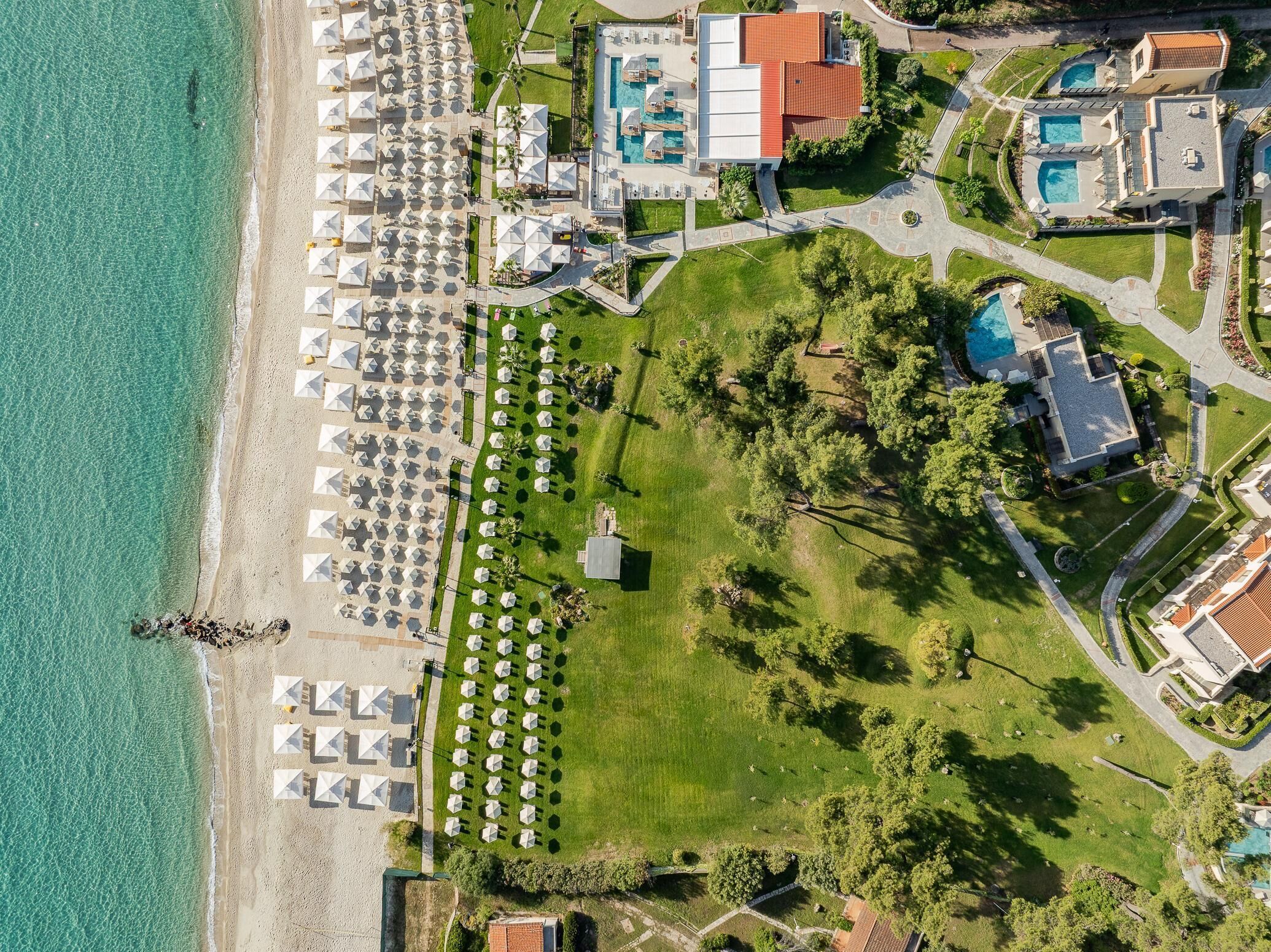 An aerial view of a resort with a beach, multiple swimming pools, and a well-maintained lawn area.