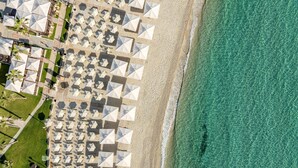 Luchtbeeld van een strandresort met rijen witte parasols en ligbedden, een zandstrand en helder turquoise water.