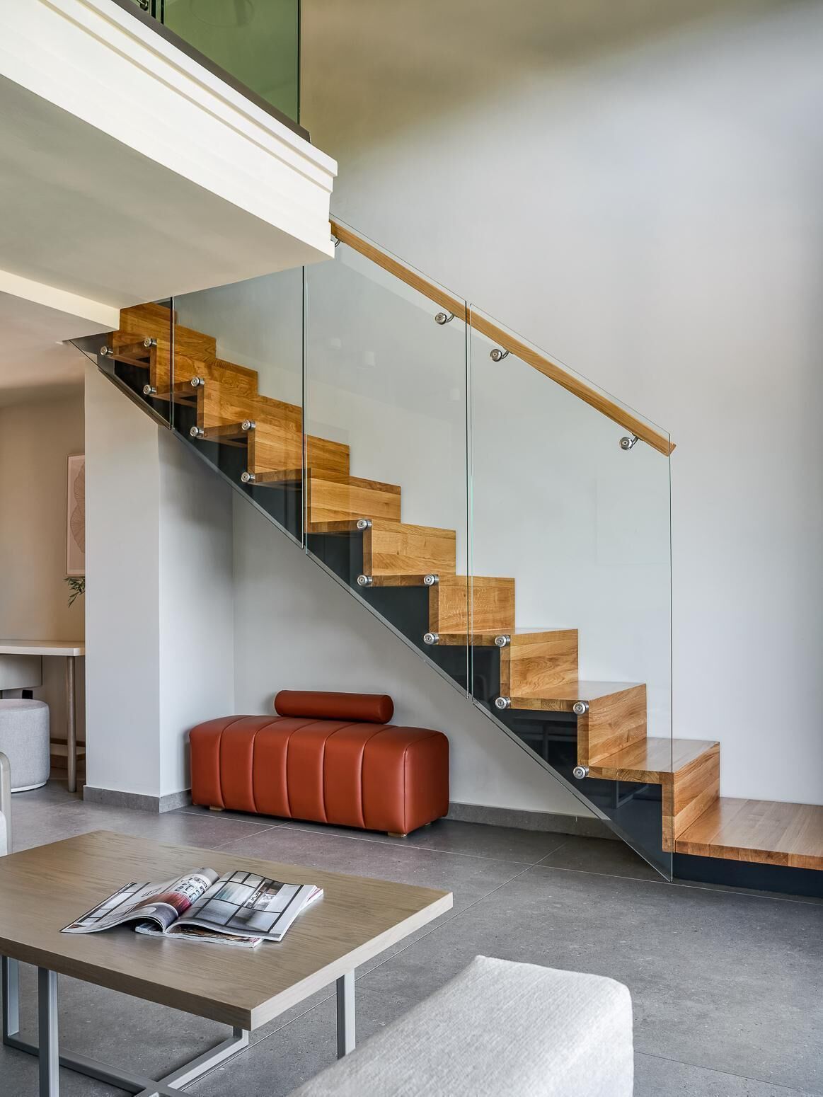 Un intérieur moderne avec un escalier en verre, un banc en cuir et une table avec des magazines.