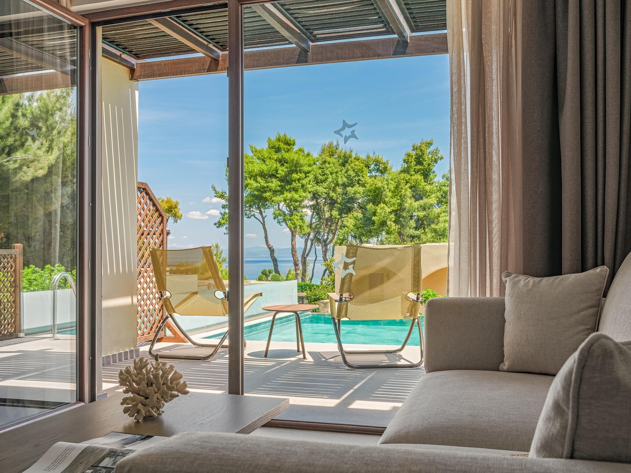 A modern room with a large glass door leading to a pool area, a sofa, and a small table with a decorative item.